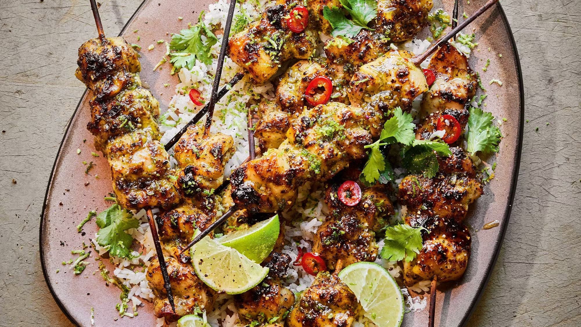 Charred Thai green curry chicken skewers piled on top of fluffy coconut jasmine rice, served with a fresh cucumber and sugar snap pea salad.
