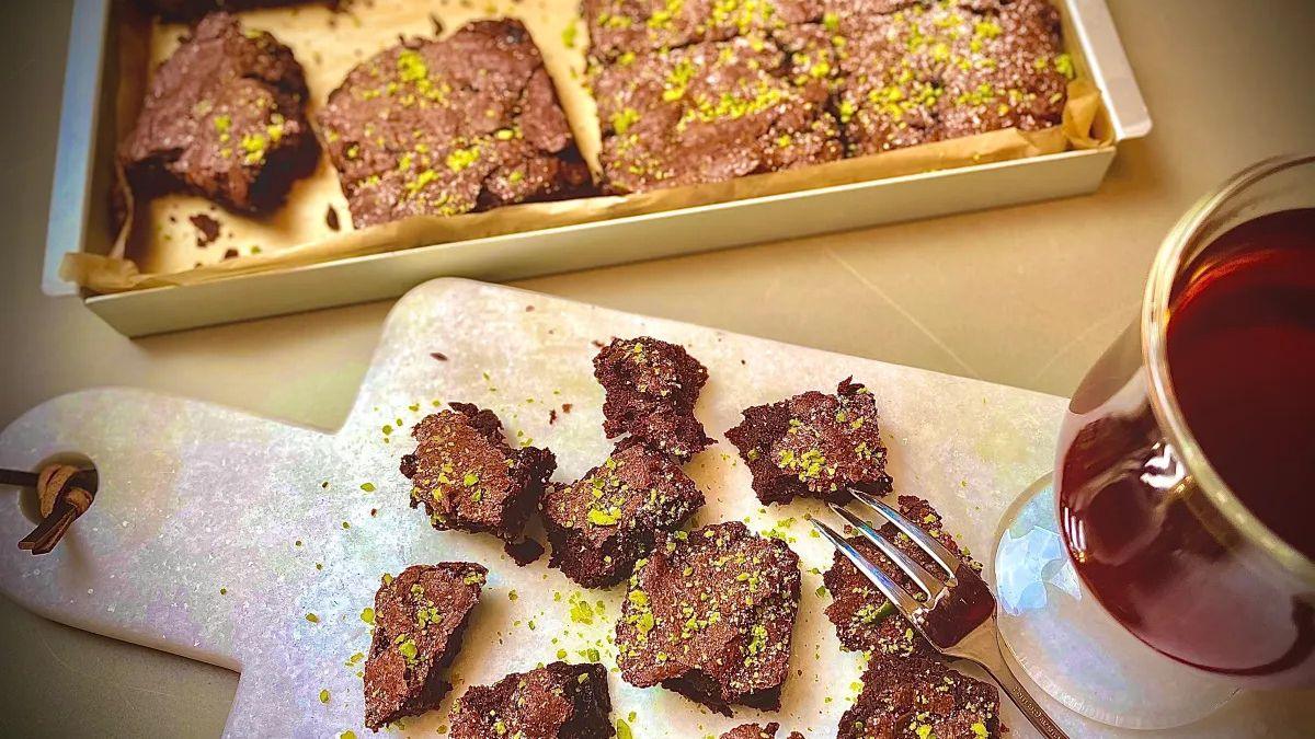 Cherry and pistachio brownies on a marble board with a glass of tea