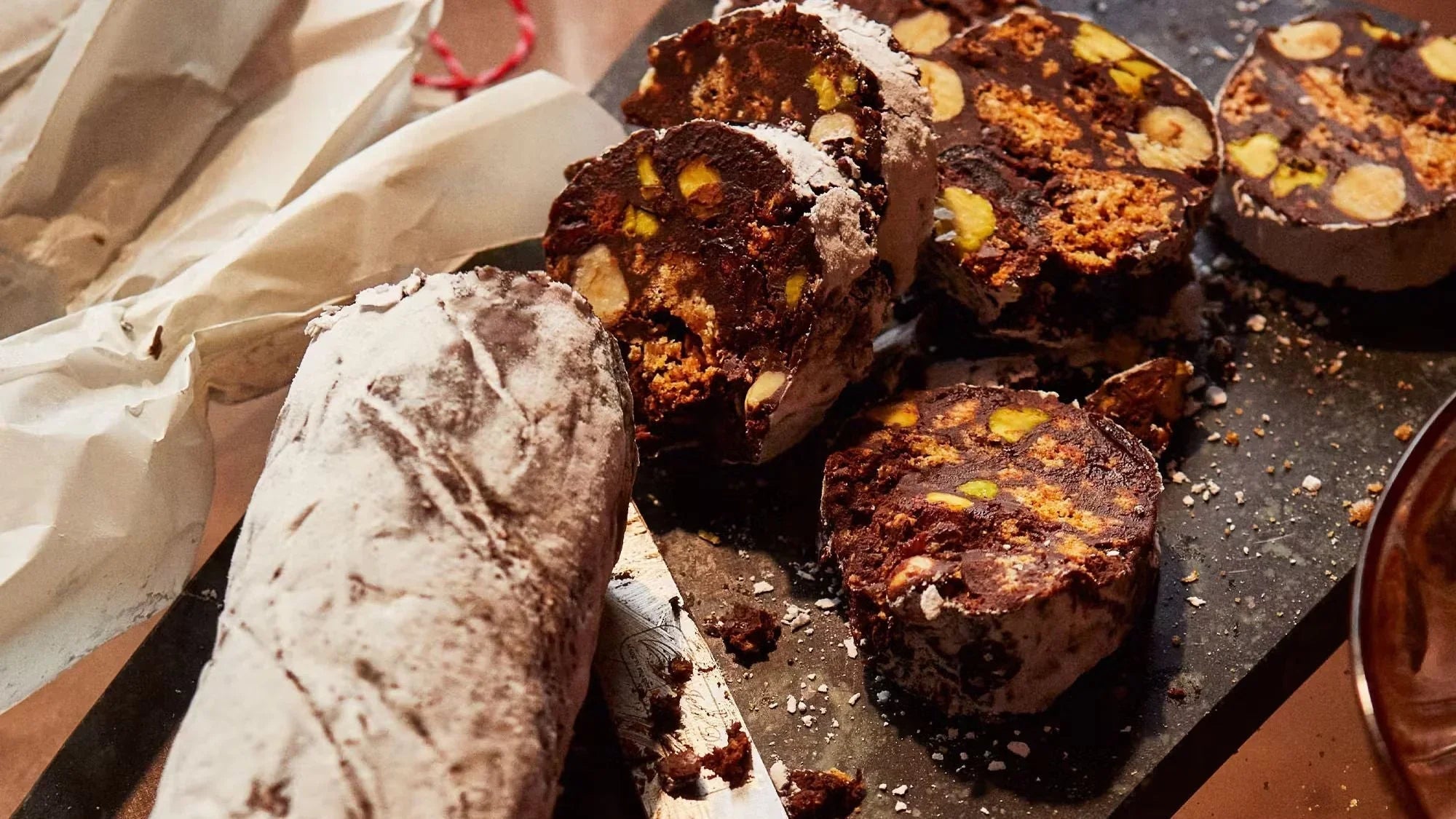 Chocolate salami dessert with nuts and biscuits, sliced on a dark serving board