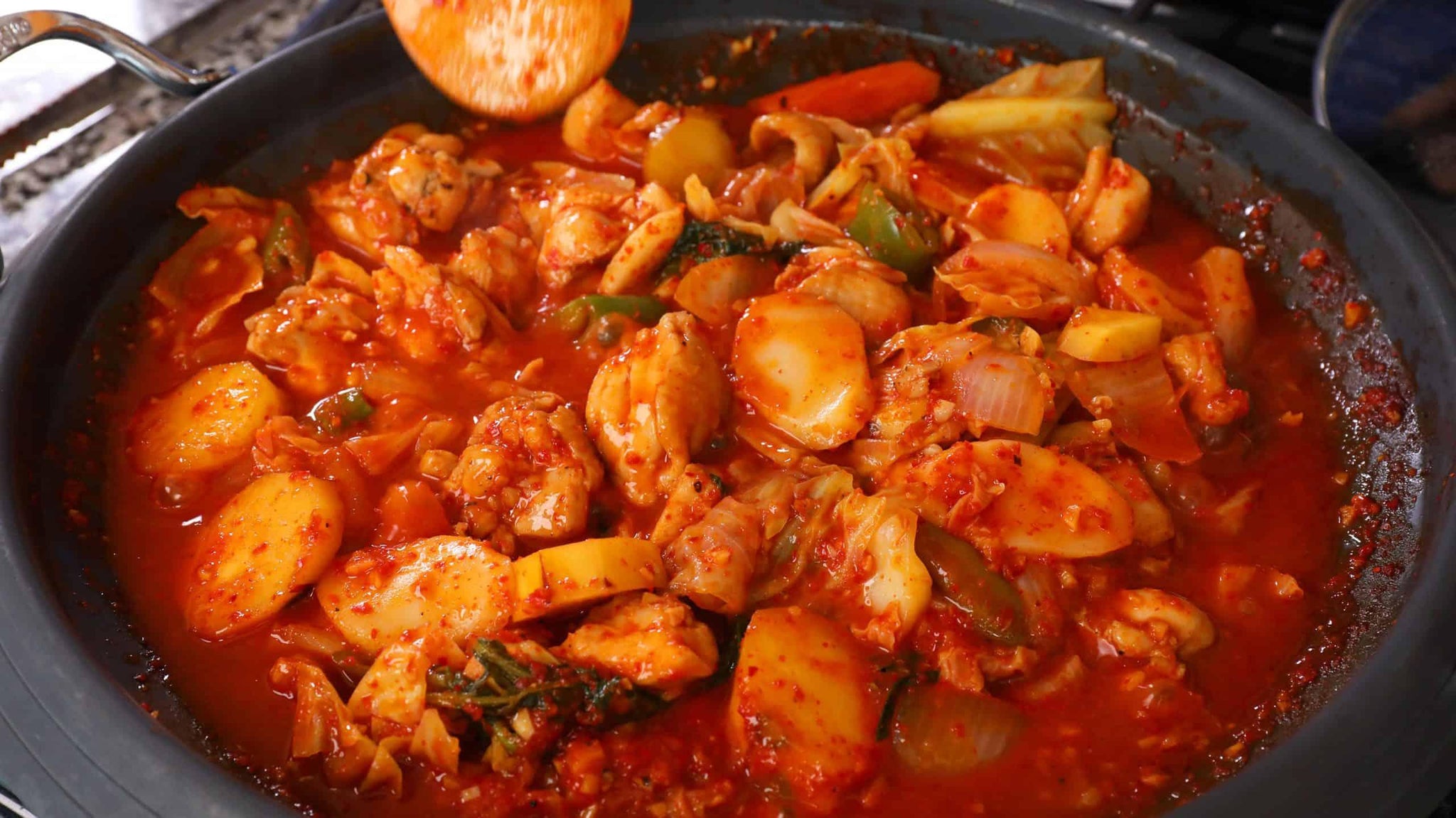 Spicy stir-fried chicken with rice cakes, vegetables, and red chili sauce in a skillet