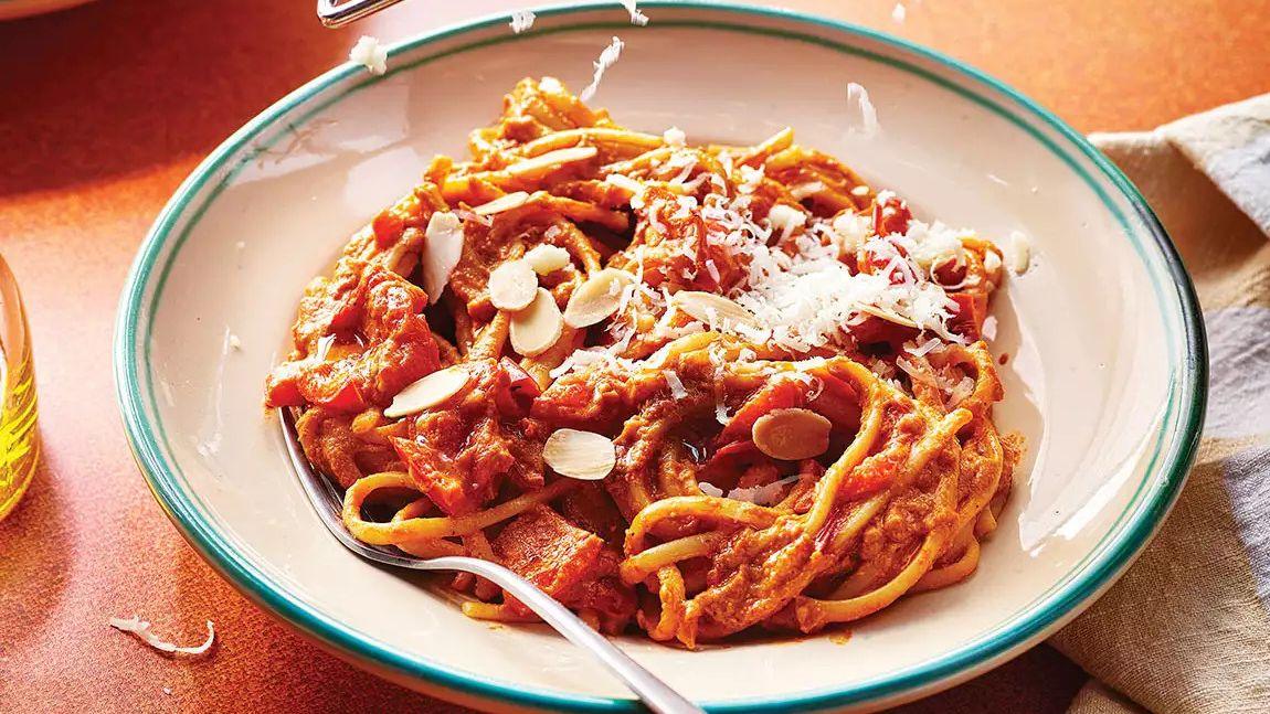 Linguine pasta with red pepper sauce, sliced almonds, and grated cheese in a bowl