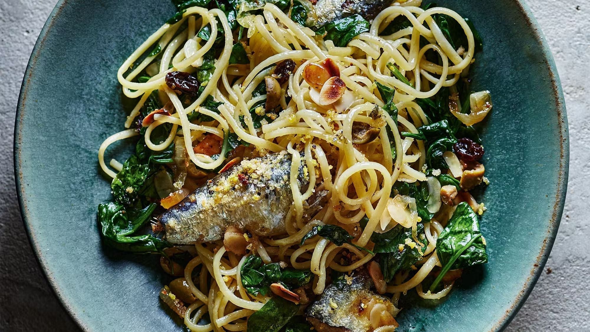 Linguine pasta with sardines, spinach, olives, and crunchy toasted crumbs in a bowl