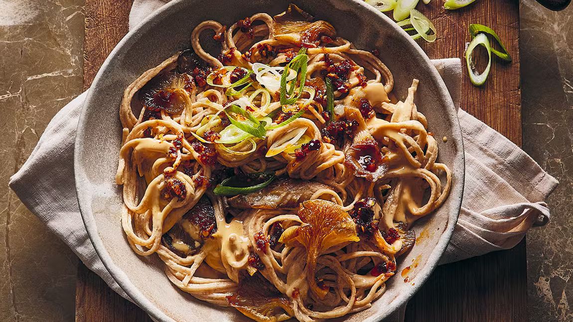 Bowl of sesame noodles topped with sticky mushrooms, chili oil, and sliced green onions