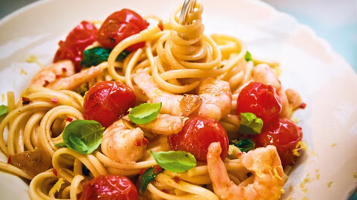 Linguine pasta with prawns, cherry tomatoes, basil, and chili on a white plate