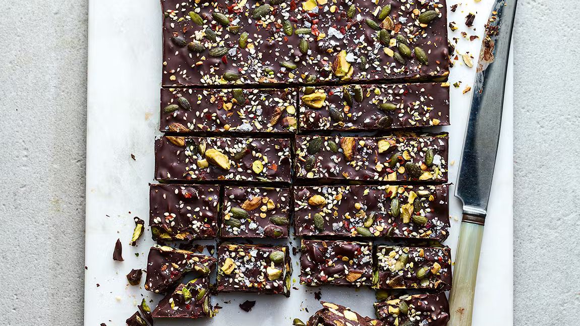 A top-down view of sliced Chilli Chocolate Tiffin bites showing toasted pistachios, pumpkin seeds, and dried apricots set in dark chocolate.