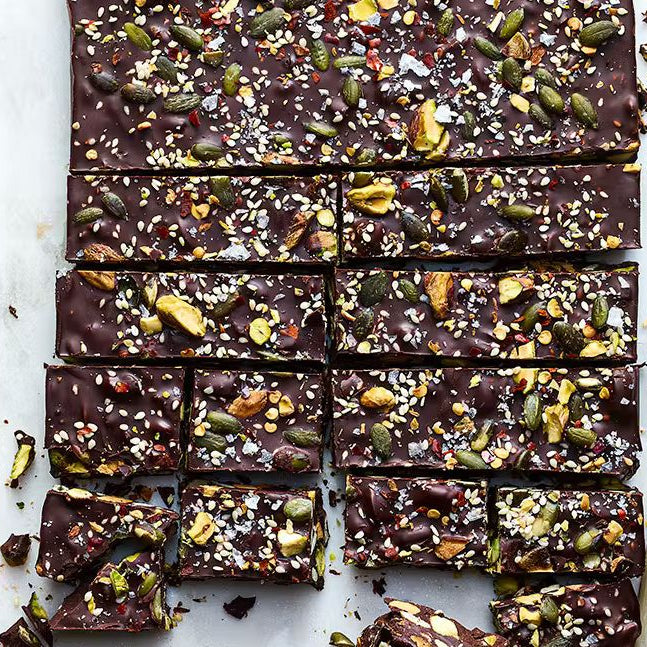 A top-down view of sliced Chilli Chocolate Tiffin bites showing toasted pistachios, pumpkin seeds, and dried apricots set in dark chocolate.