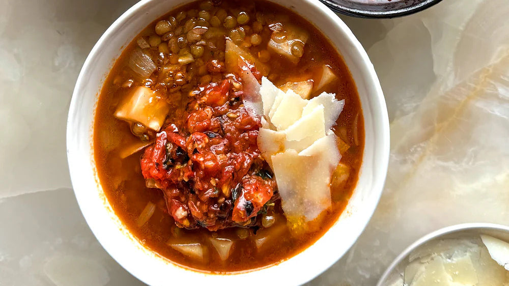 Hearty lentil soup with tomato topping, diced vegetables, and shaved cheese in a white bowl