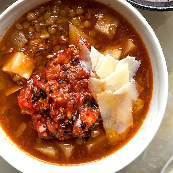 Hearty lentil soup with tomato topping, diced vegetables, and shaved cheese in a white bowl
