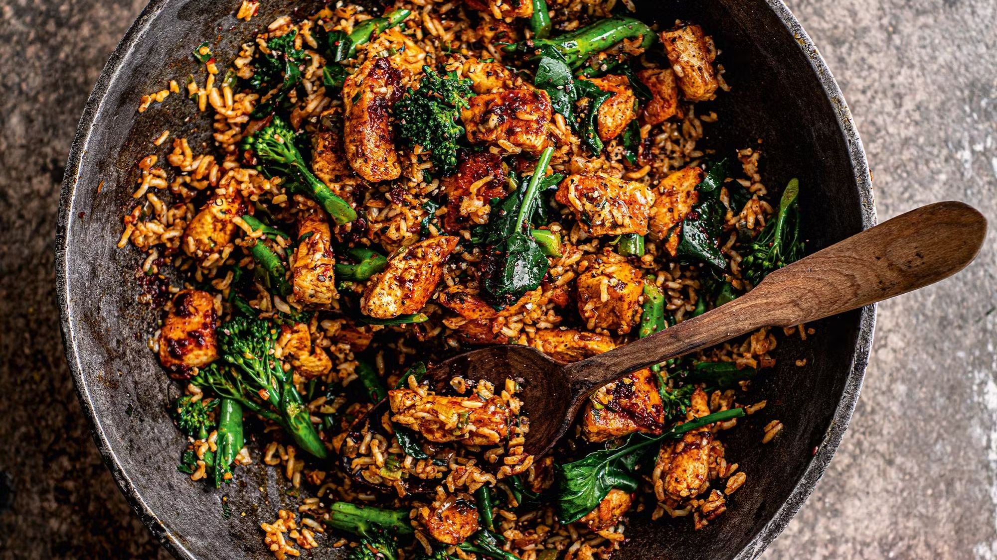 A pan of spicy chicken fried rice with tenderstem broccoli, chicken breast, and harissa paste.