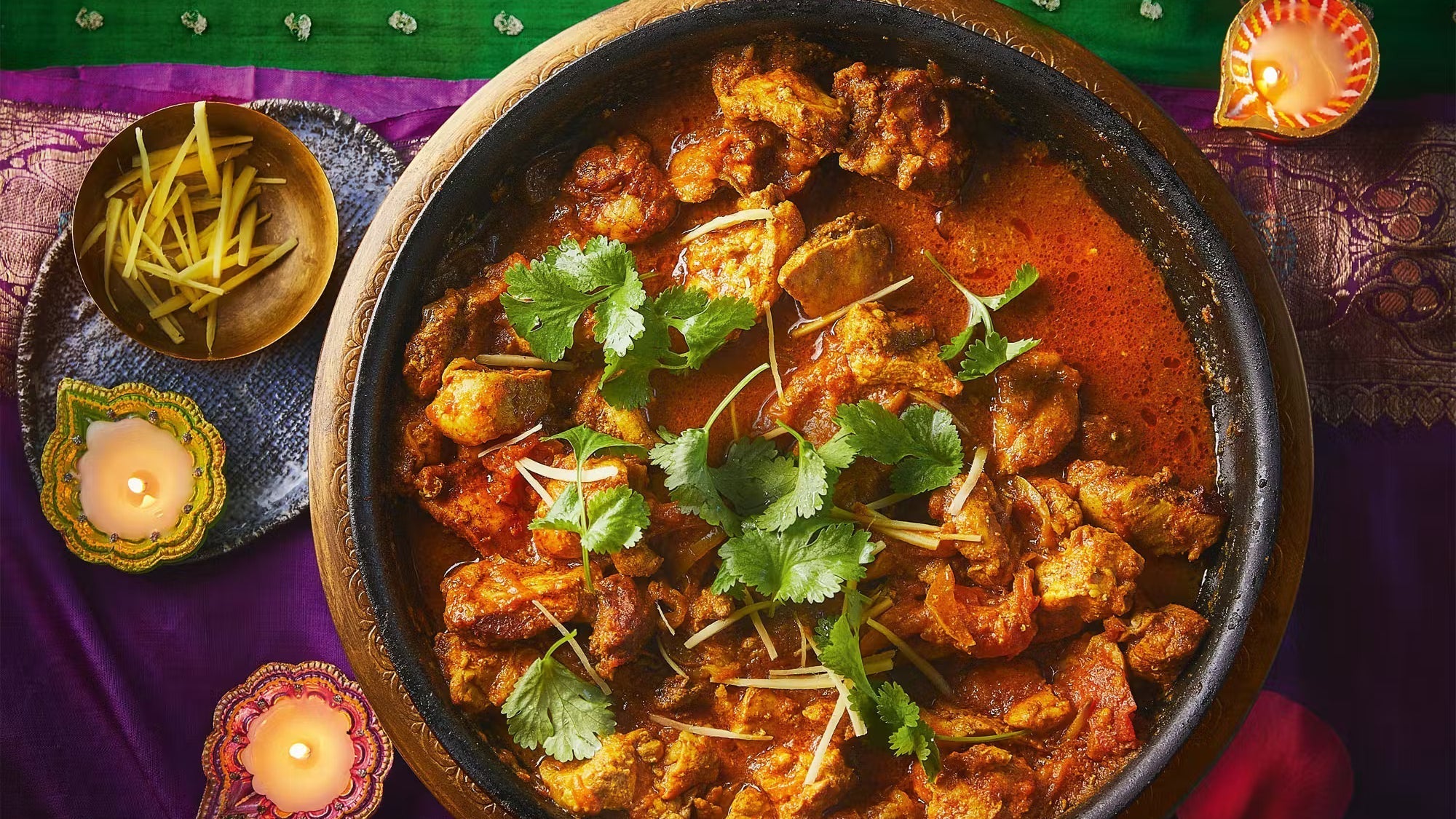 Traditional chicken karahi curry garnished with cilantro and ginger, served in a black pot with festive candles and sliced ginger on the side.