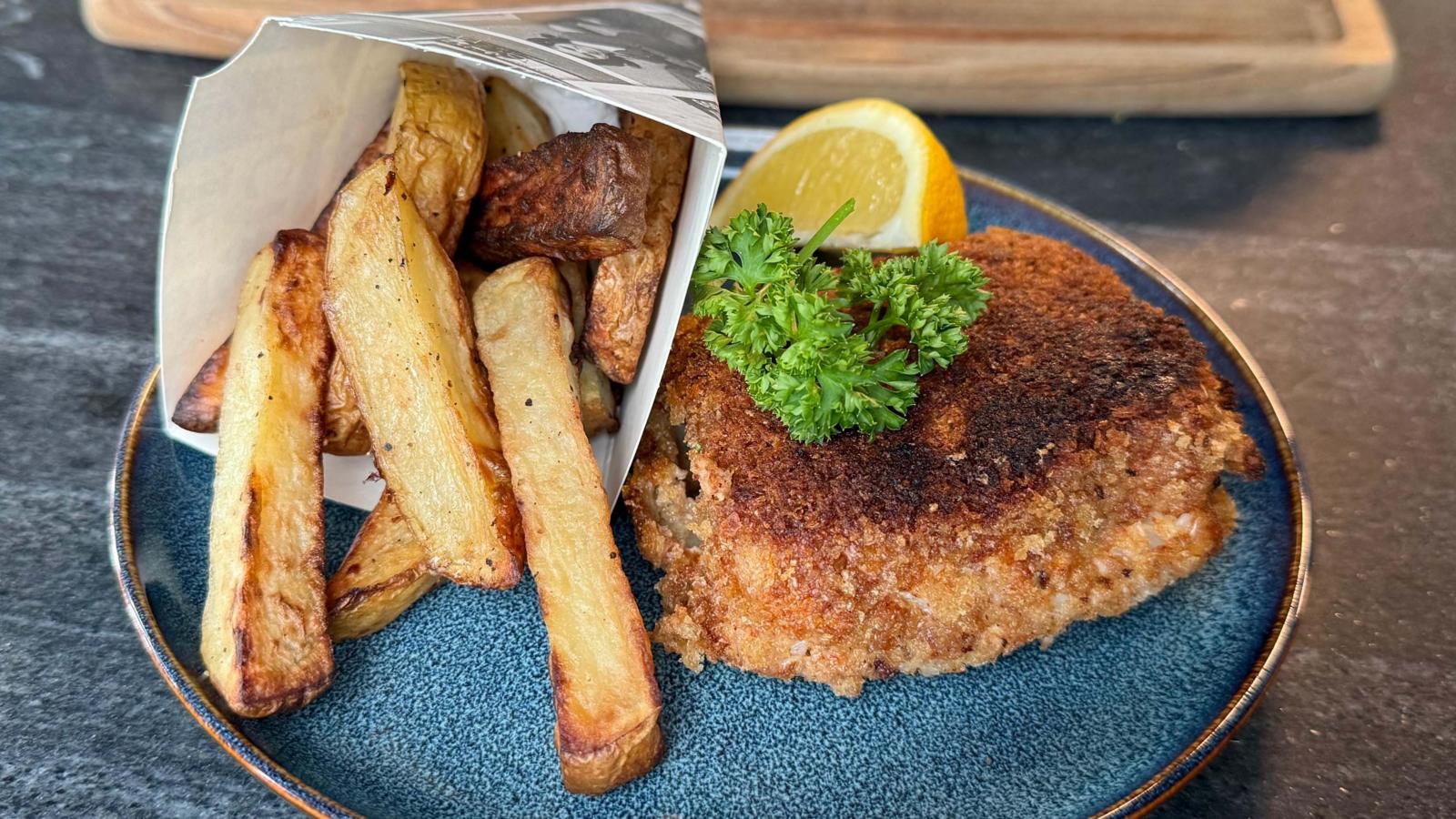 Crispy spiced curried fish fillets served with golden air-fried thick-cut chips, vibrant minty mashed peas, and a fresh lemon wedge on a plate.