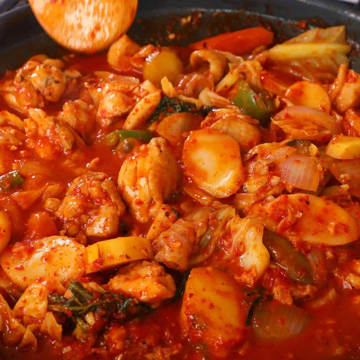 Spicy stir-fried chicken with rice cakes, vegetables, and red chili sauce in a skillet
