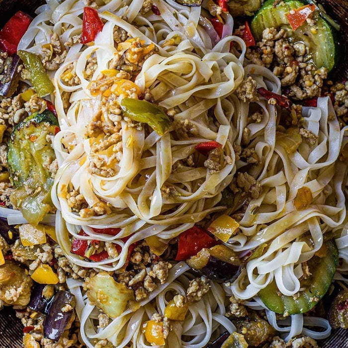 Chilli spiced pork with rice noodles, colorful peppers, zucchini and eggplant in a rustic bowl