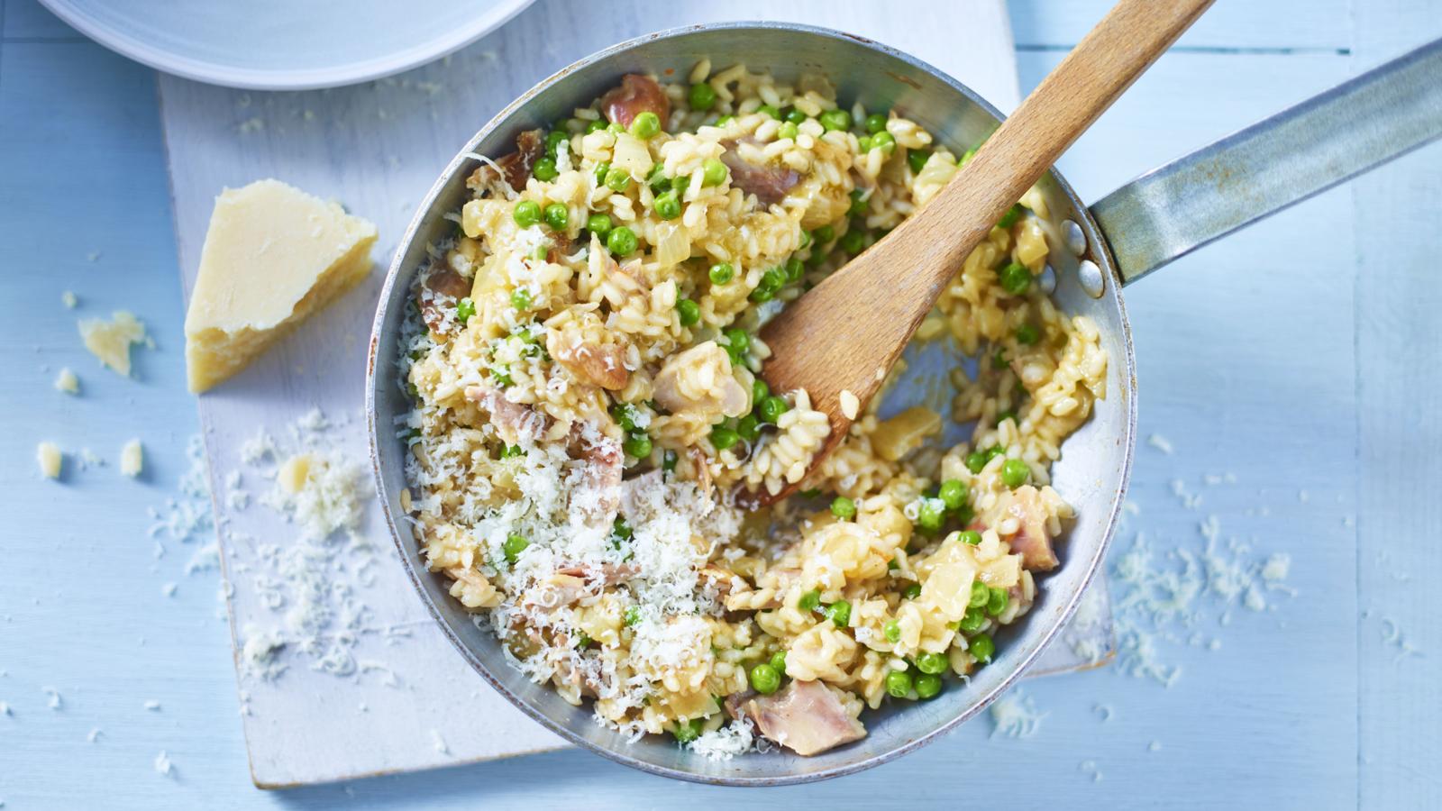 Creamy chicken and pea risotto topped with grated cheese in a pan on a blue background