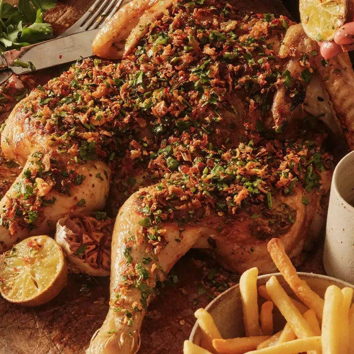 Herb butter roasted spatchcock chicken garnished with fresh parsley and served with fries