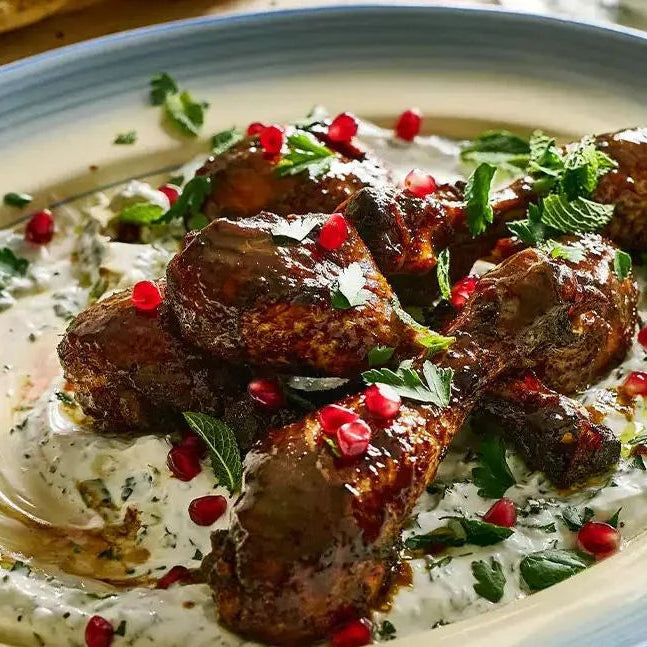 Pomegranate and honey glazed chicken drumsticks on herbed yogurt, garnished with mint and pomegranate seeds