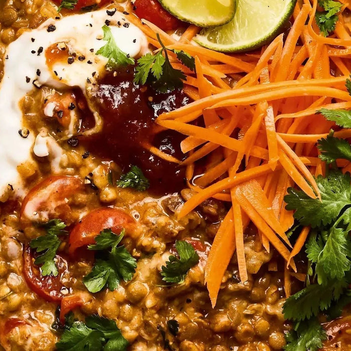 Tomato coconut dal with sliced carrots, fresh coriander, sauce, and lime wedges on a plate
