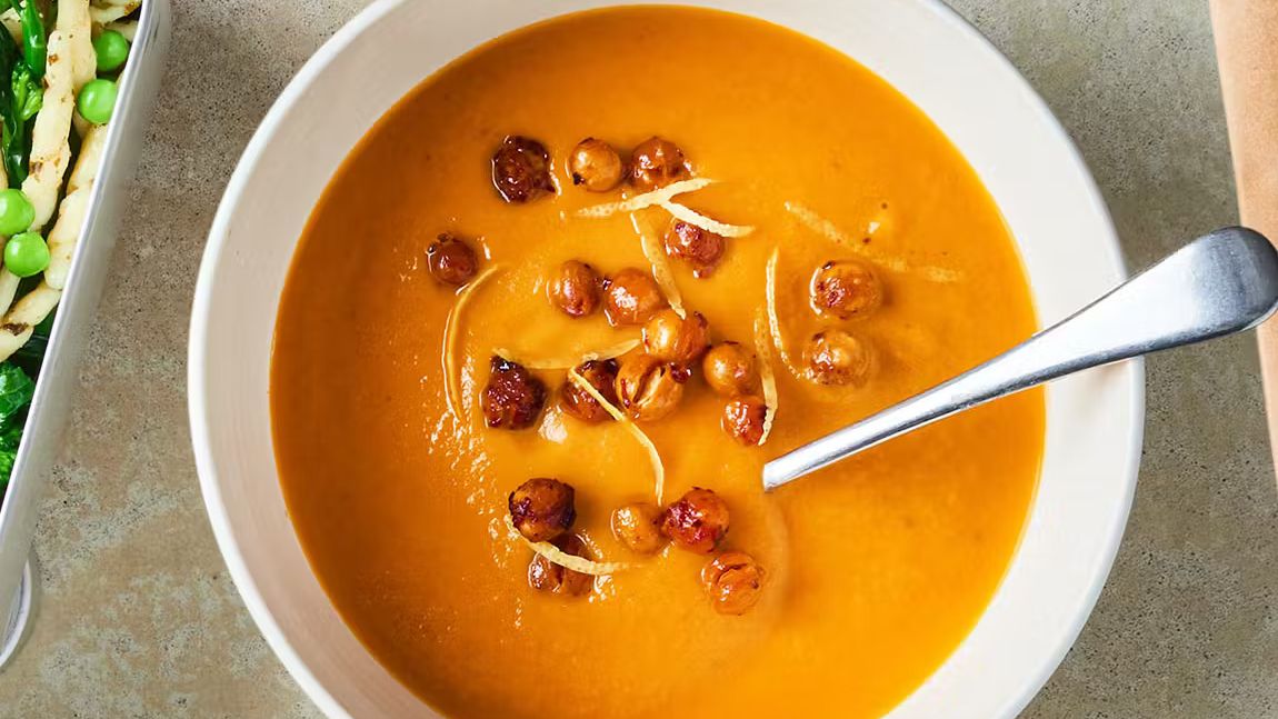Roasted carrot harissa chickpea soup topped with crispy chickpeas and lemon zest in a bowl