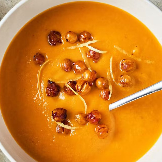 Roasted carrot harissa chickpea soup topped with crispy chickpeas and lemon zest in a bowl
