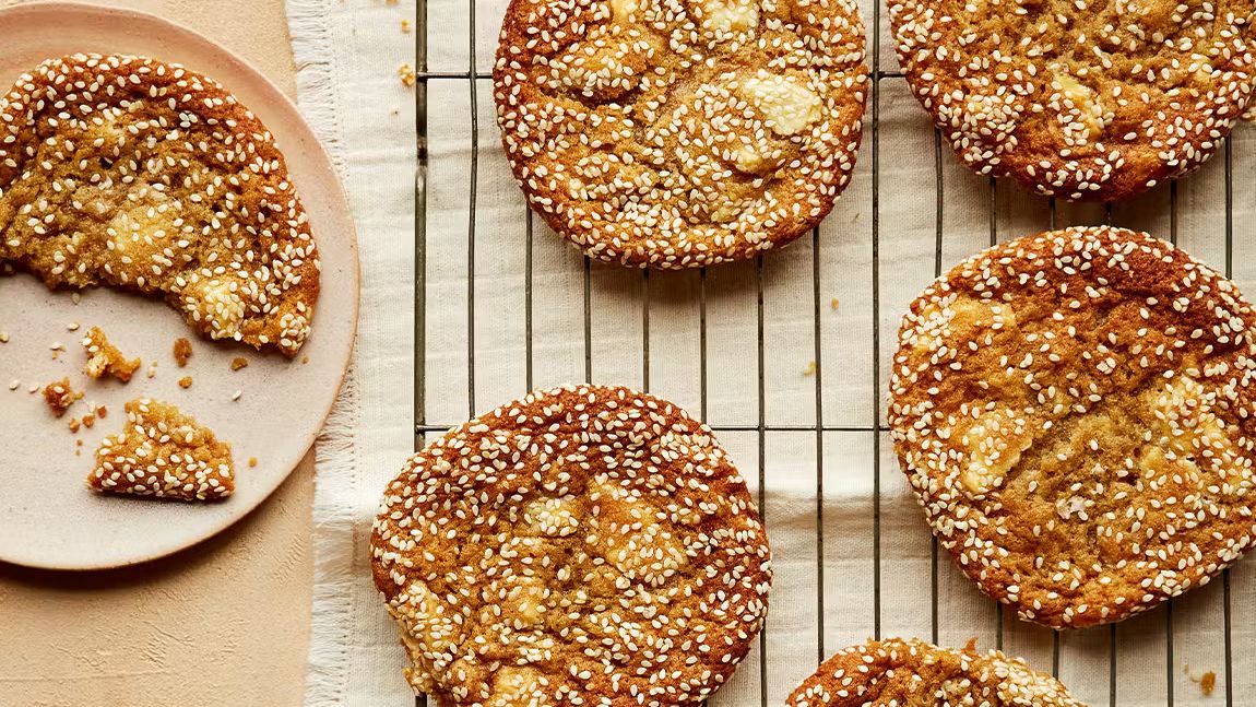 Sesame miso cookies with golden edges on a cooling rack and plate, sprinkled with sesame seeds