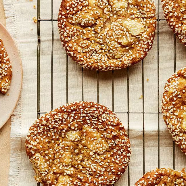 Sesame miso cookies with golden edges on a cooling rack and plate, sprinkled with sesame seeds