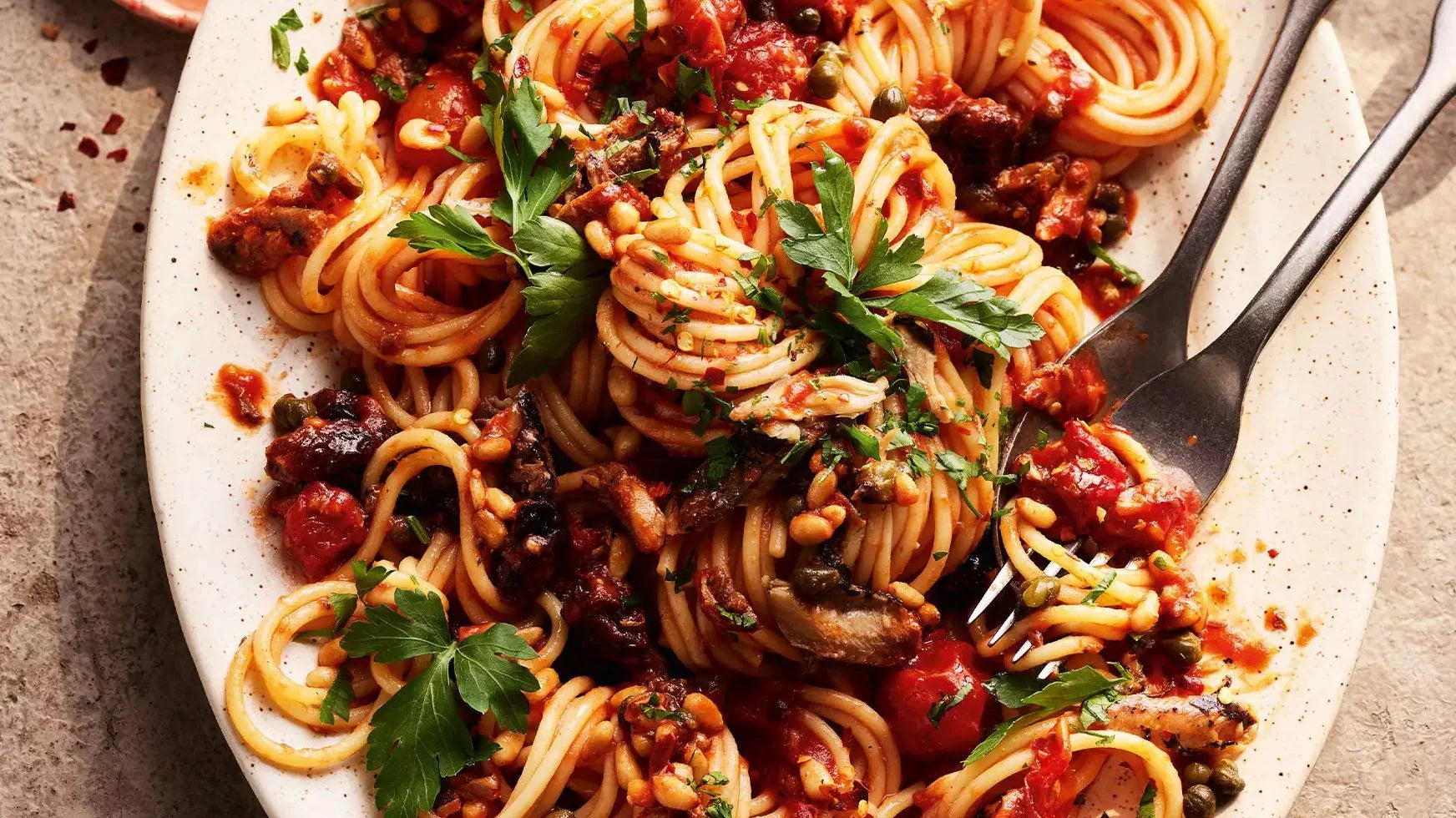 Sicilian sardine pasta with tomato sauce, pine nuts, capers, and parsley on a plate