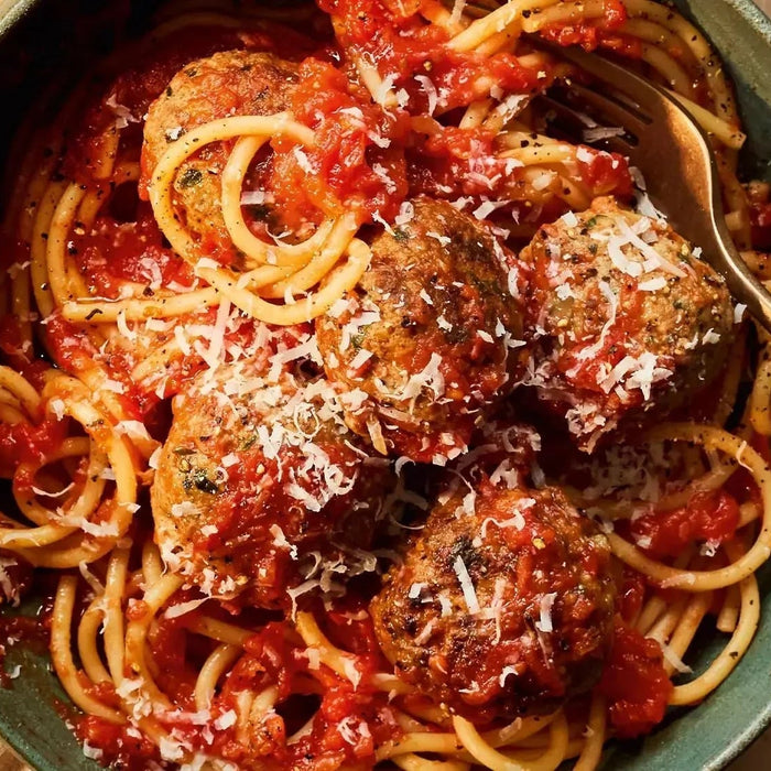 Spaghetti and meatballs topped with tomato sauce and grated cheese in a rustic bowl