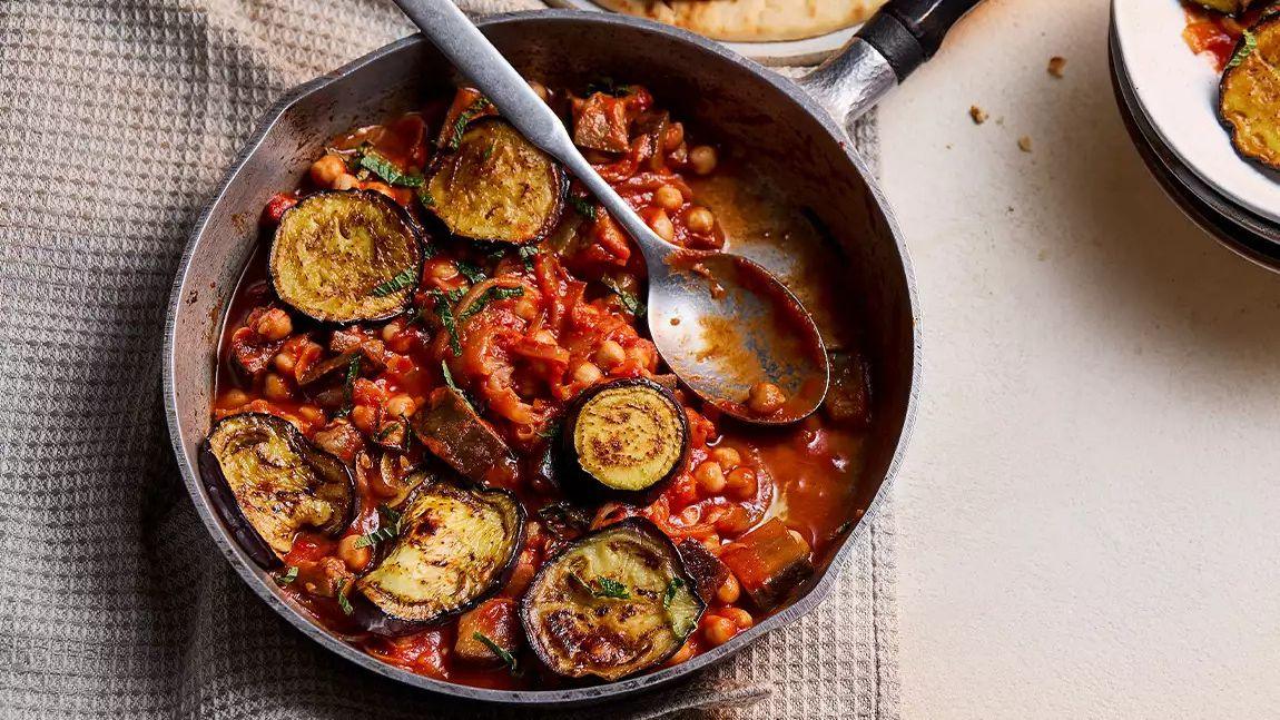 Spiced aubergine and chickpea tomato stew in a pan, garnished with fresh herbs