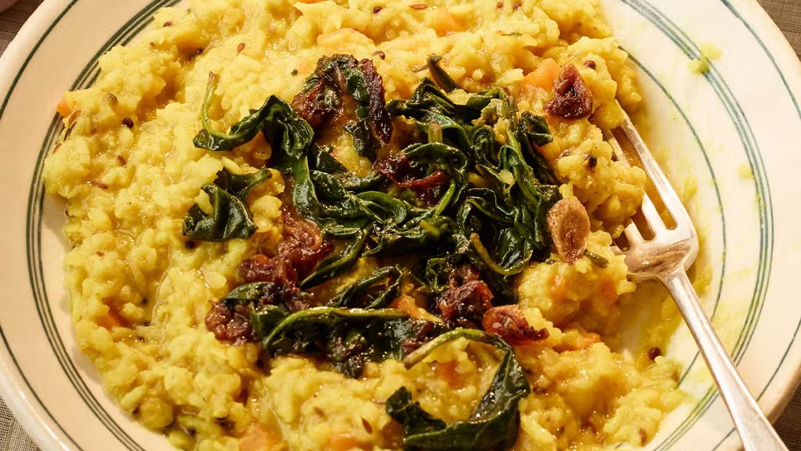 Bowl of spiced lentil and rice stew topped with sautéed greens and caramelized onions