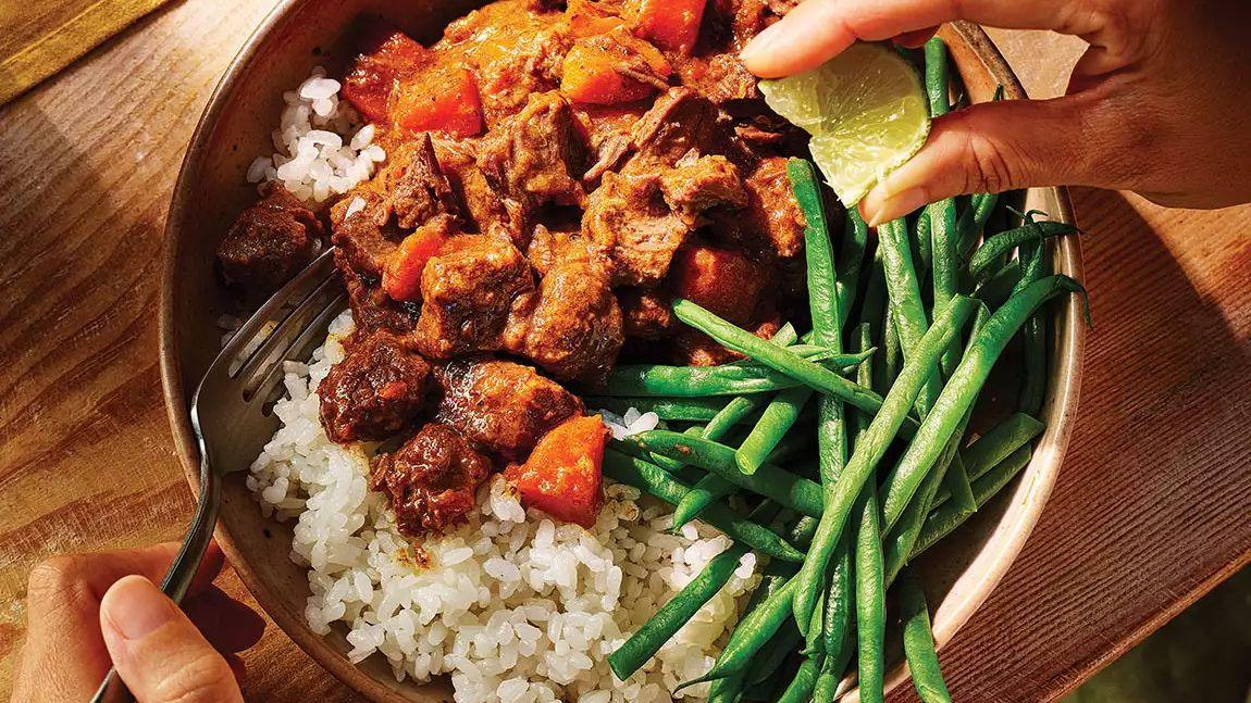 Beef stew with carrots over rice, fresh green beans, hand squeezing lime, rustic table setting