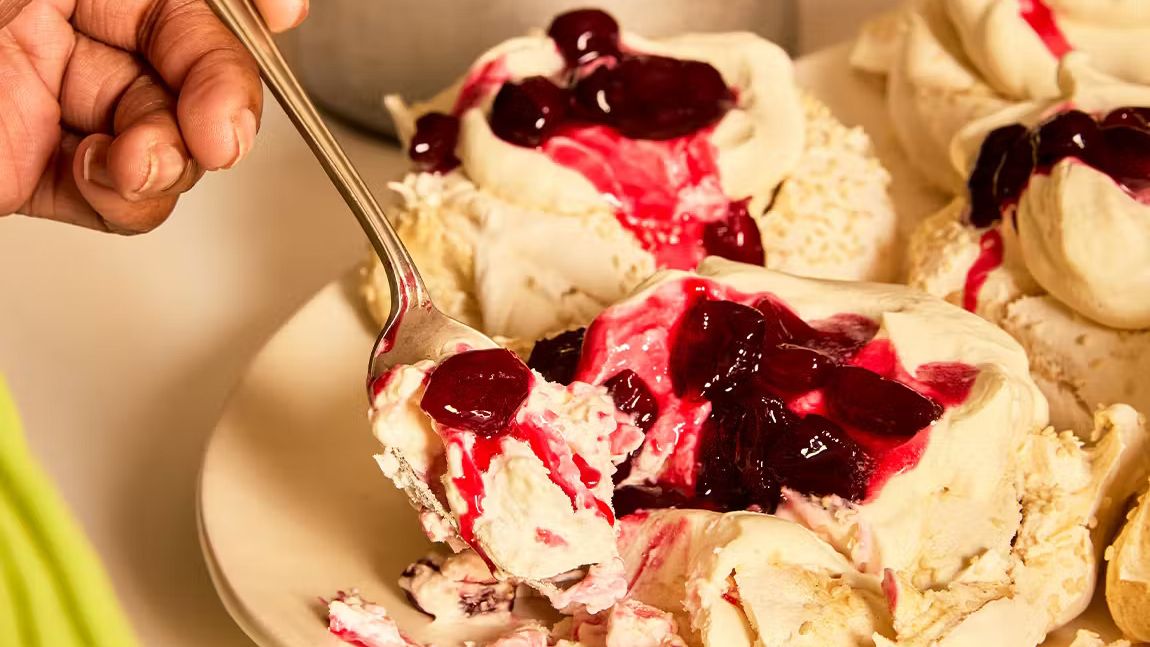 A platter of large marbled tahini meringues topped with whipped cardamom cream and a glossy, dark red cherry compote.