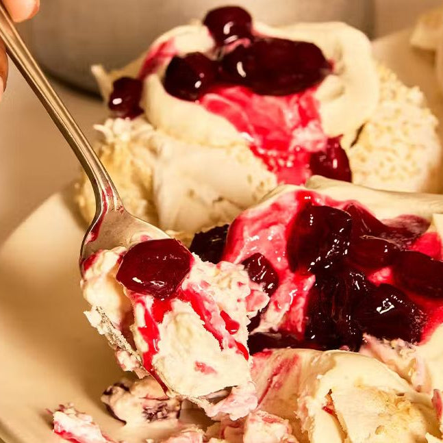 A platter of large marbled tahini meringues topped with whipped cardamom cream and a glossy, dark red cherry compote.