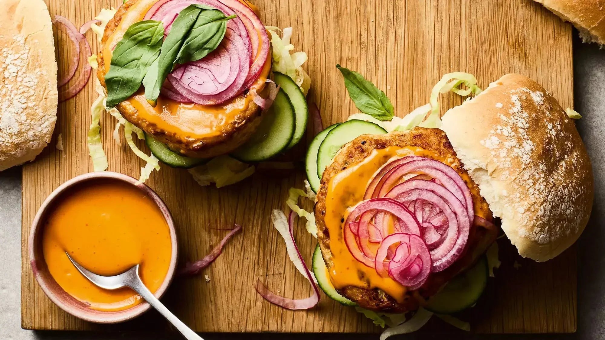 Thai spiced chicken burgers with lettuce, sliced cucumber, pickled onions, and orange sauce on wooden board