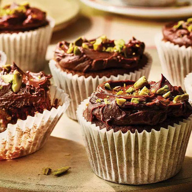 Pistachio chocolate cupcakes topped with chopped pistachios on a wooden tray