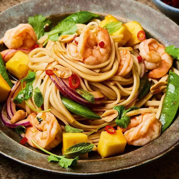 Prawn and mango salad with noodles, snap peas, red onion, herbs, and chili in a rustic bowl