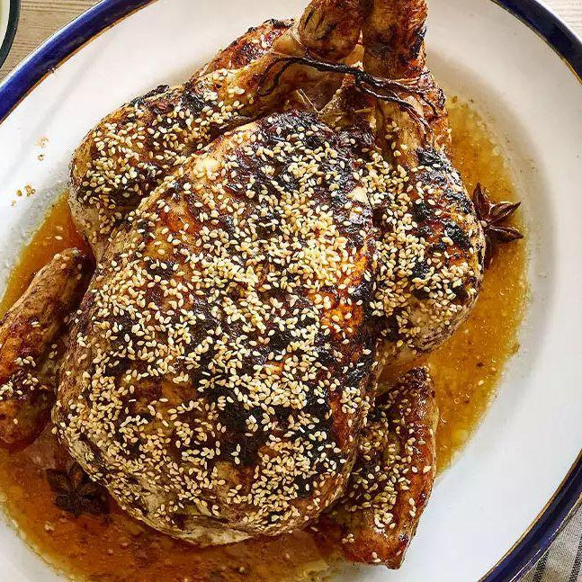 Sesame soy roast chicken on a platter with sauce, served with rice and green relish.