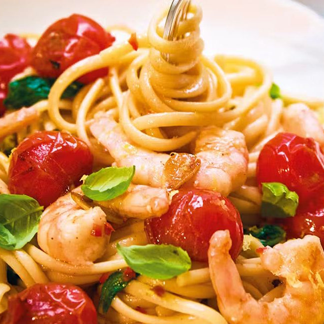 Linguine pasta with prawns, cherry tomatoes, basil, and chili on a white plate