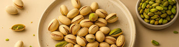 Pistachio nuts in shells on a ceramic plate, with a bowl of shelled pistachios nearby