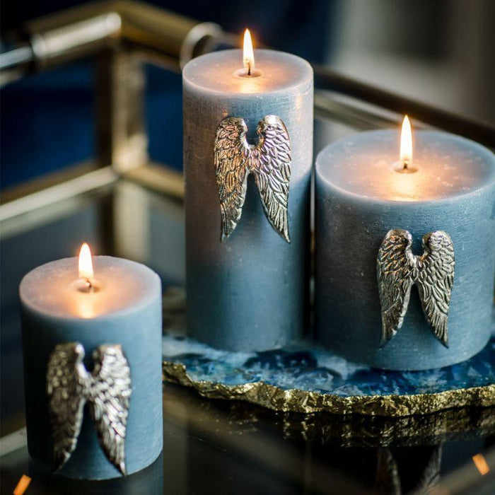 Set of three blue candles with metal angel wing pins, lit and arranged on a glass tray